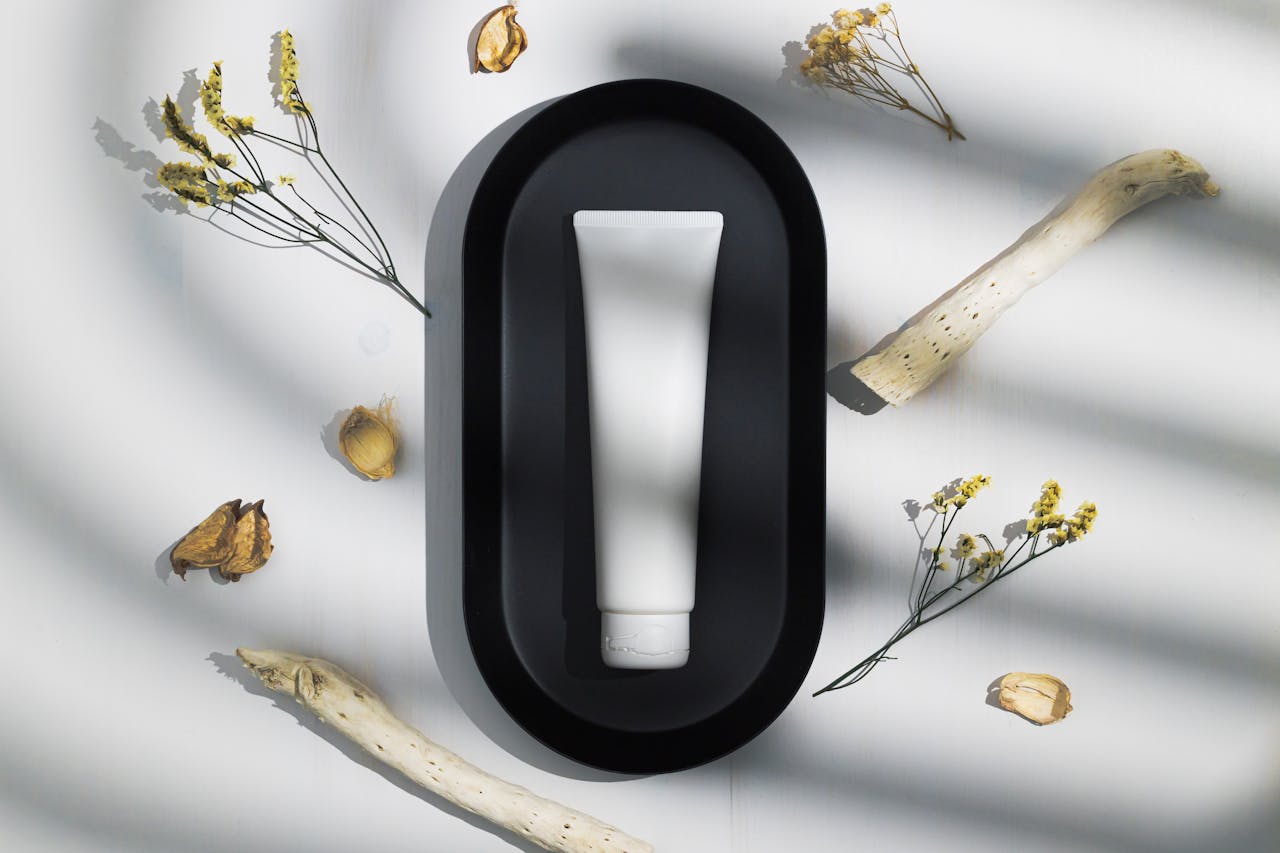 hero-img-02 Elegant skincare tube on black tray surrounded by dried natural elements under soft shadows.